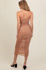 woman wearing a tan strapless maternity dress with ruched details and a midi length, showing off a baby bump from the back