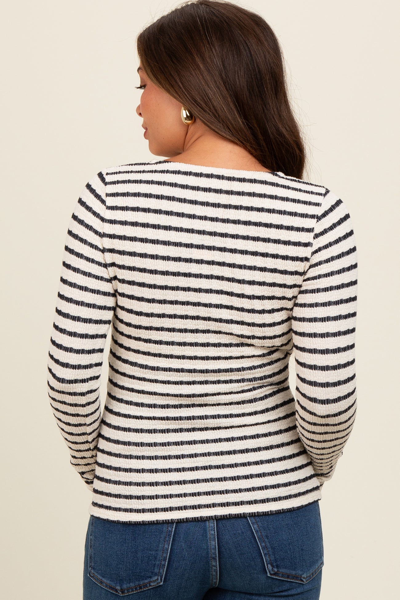 woman wearing a black and white striped long sleeve maternity top, seen from the back, paired with blue jeans