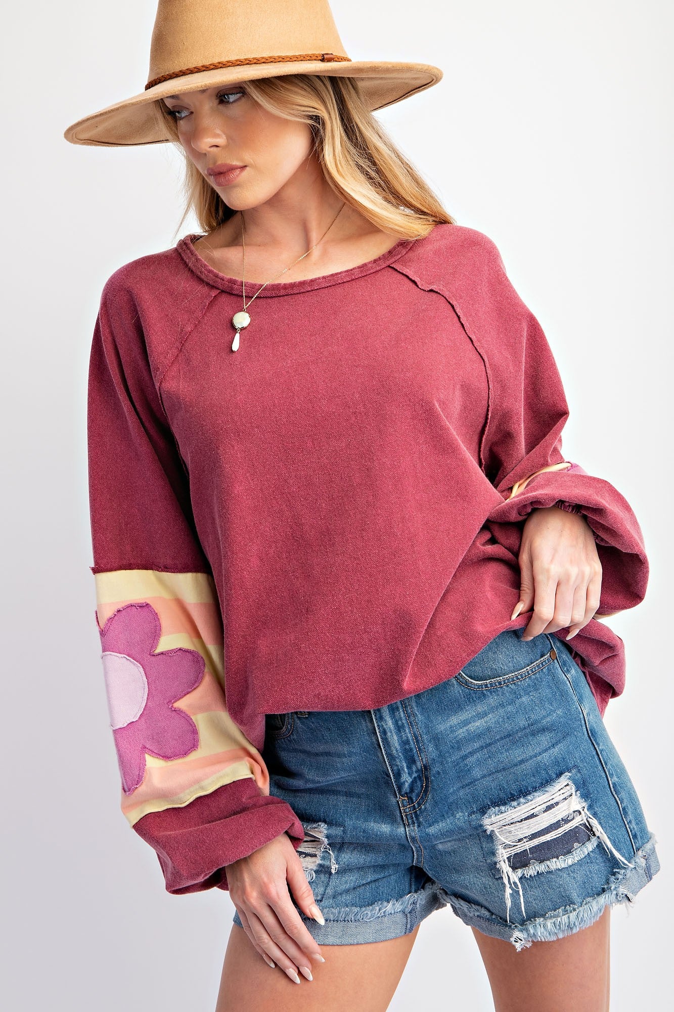 woman wearing a burgundy oversized sweatshirt with a floral design on the sleeves and distressed denim shorts