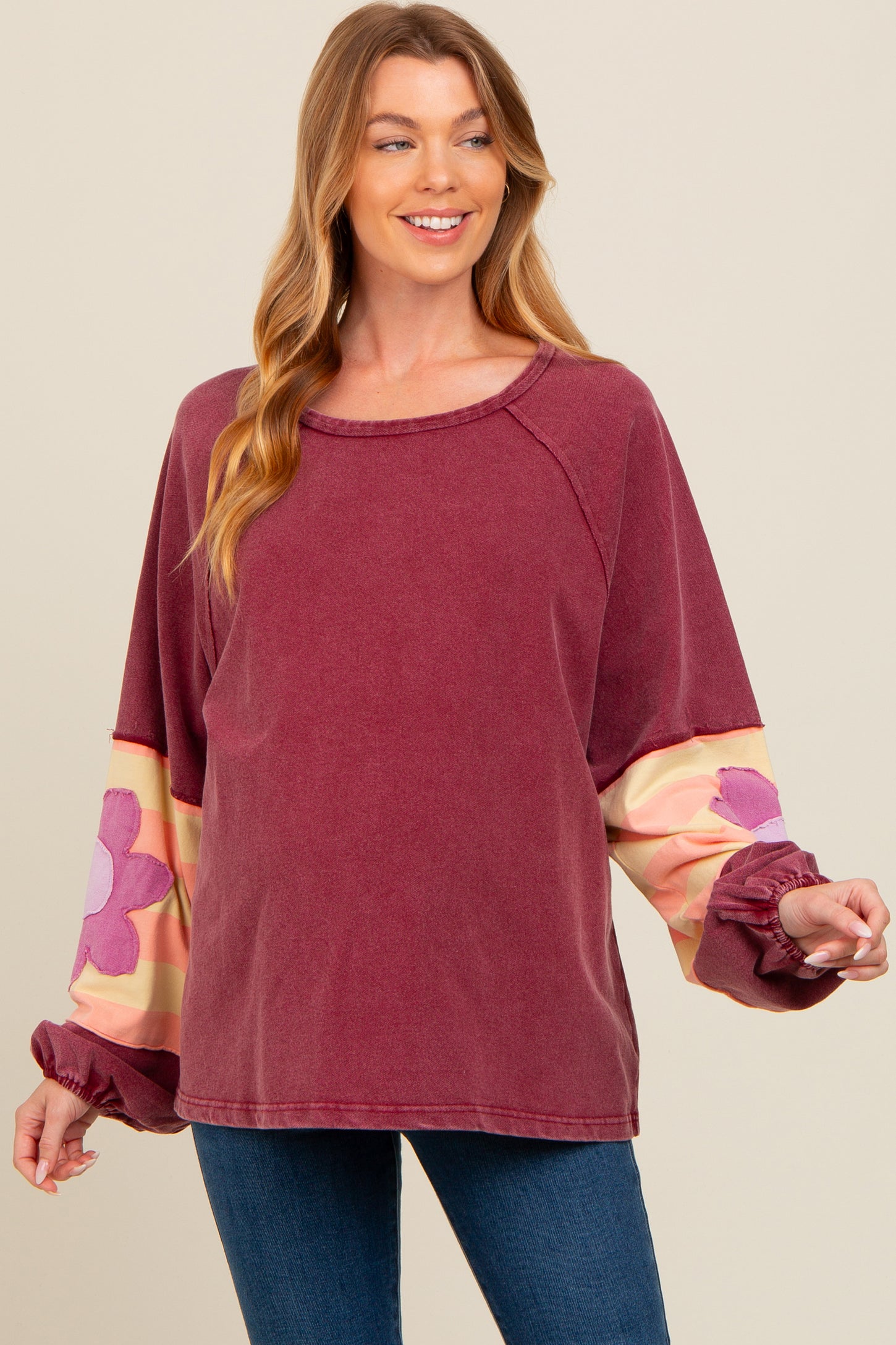 woman wearing a burgundy maternity sweatshirt with floral sleeves and a relaxed fit, holding her baby bump