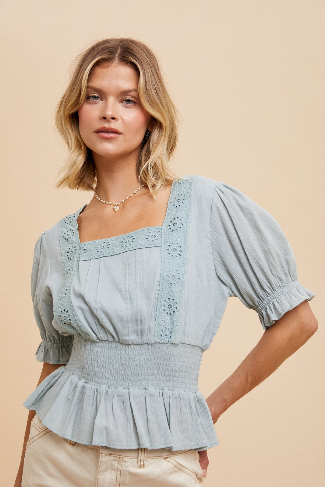woman wearing a light blue smocked peplum top with lace detailing and puff sleeves