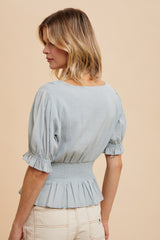 woman wearing a light blue peplum top with puff sleeves and a smocked waist, shown from the back