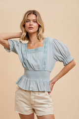 woman wearing a light blue peplum top with lace detailing and short puff sleeves, styled with beige shorts