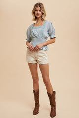 woman wearing a light blue puff sleeve blouse with lace detail and cream shorts, paired with brown cowboy boots