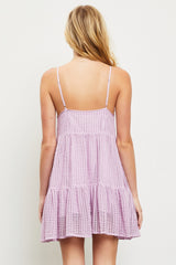 woman wearing a light purple sleeveless dress with a tiered hem and a textured fabric, showing the back view