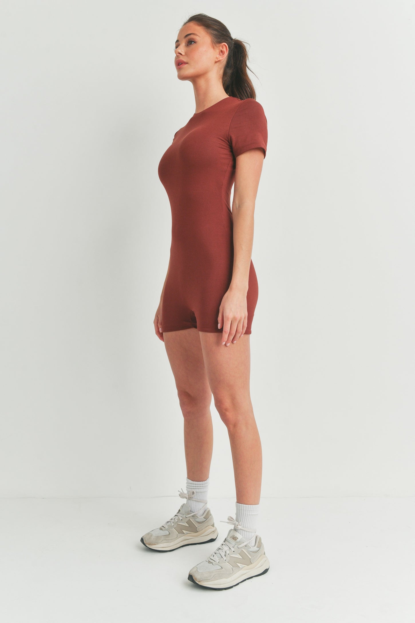 woman wearing a rust-colored short sleeve bodysuit with a fitted style and athletic shoes