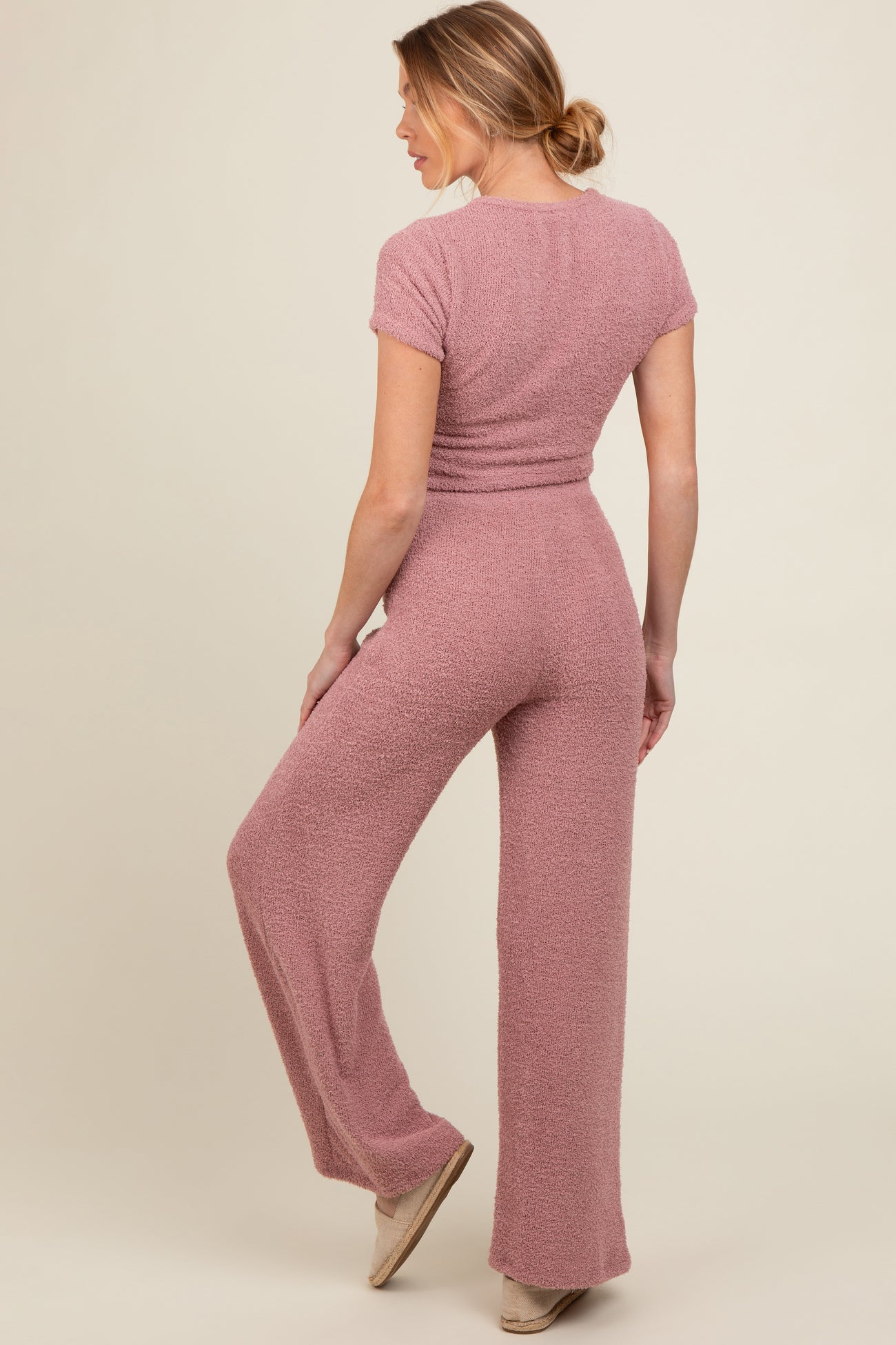 woman wearing a pink textured maternity jumpsuit, showing a relaxed fit and wide-leg style from the back