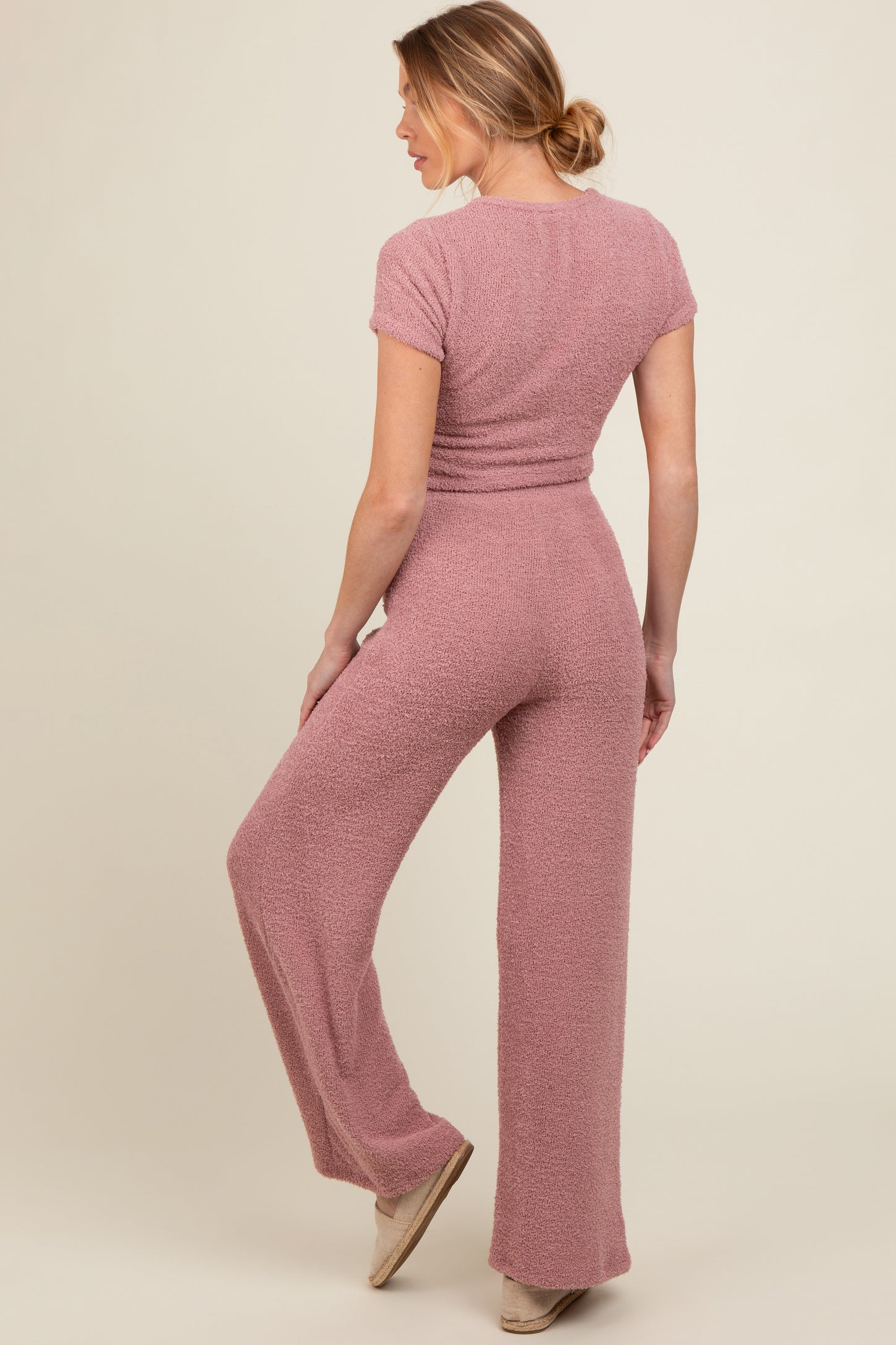 woman wearing a pink textured maternity jumpsuit, showing a relaxed fit and wide-leg style from the back