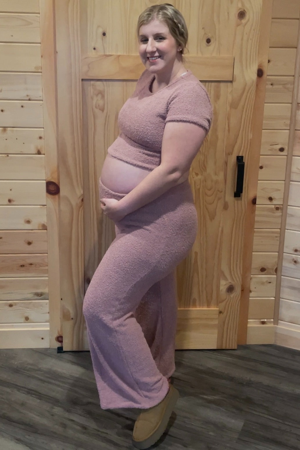 woman wearing a light pink maternity two-piece loungewear set and holding her baby bump