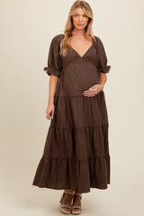 woman wearing a dark brown maternity maxi dress with tiered ruffles and puff sleeves, holding her baby bump