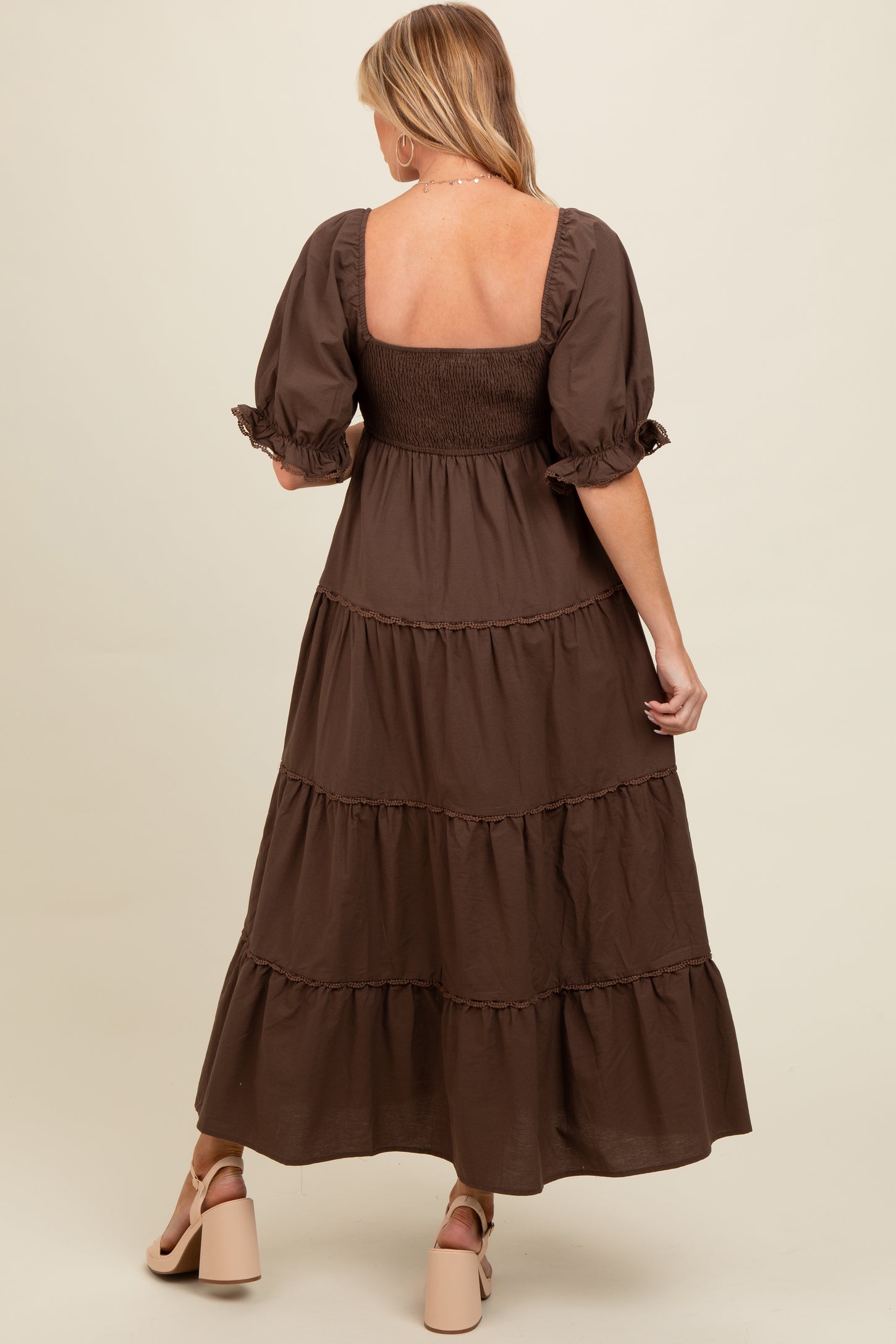 woman wearing a brown tiered maternity maxi dress with puff sleeves and a smocked bodice