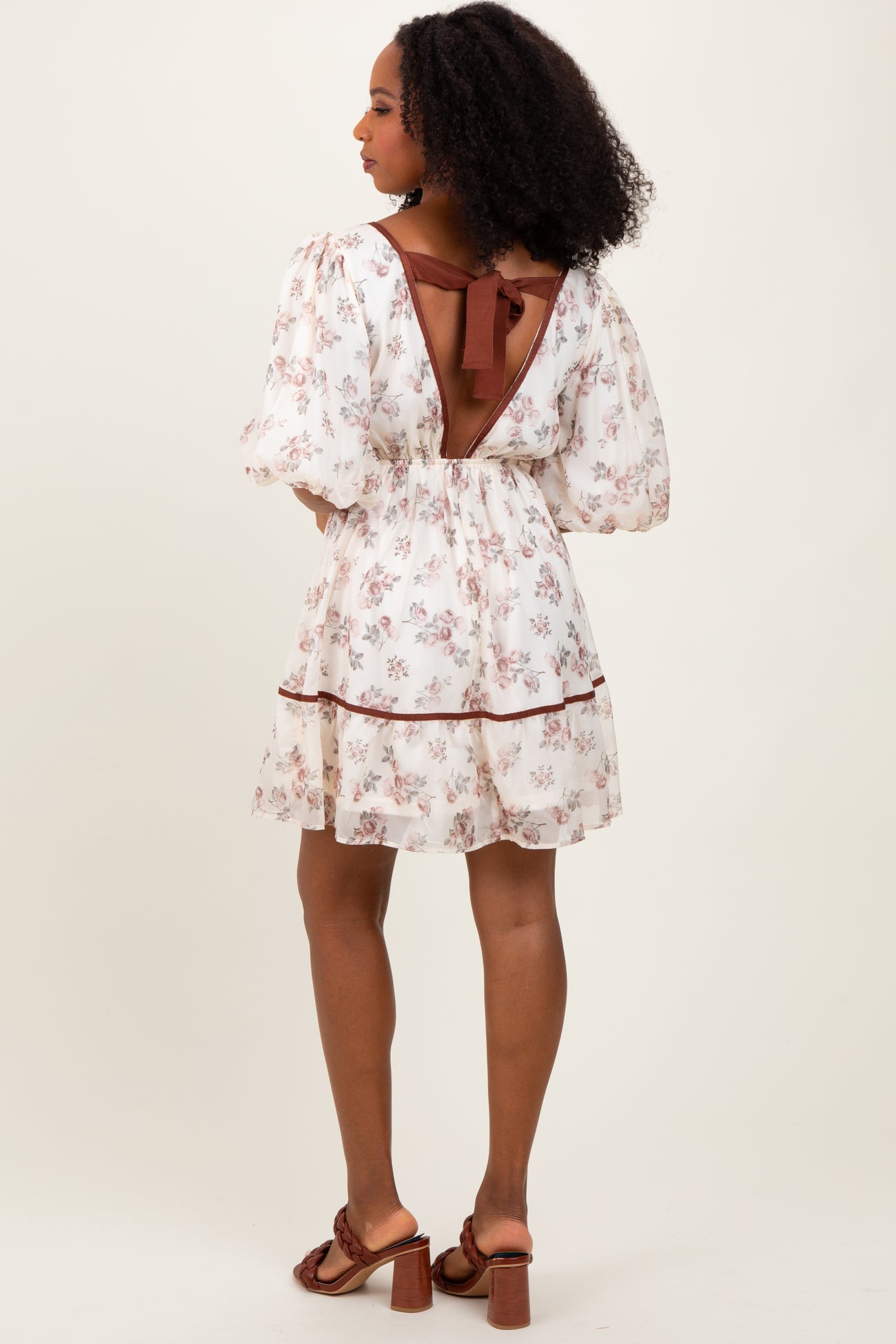 woman wearing a floral white short dress with puff sleeves and a back tie detail
