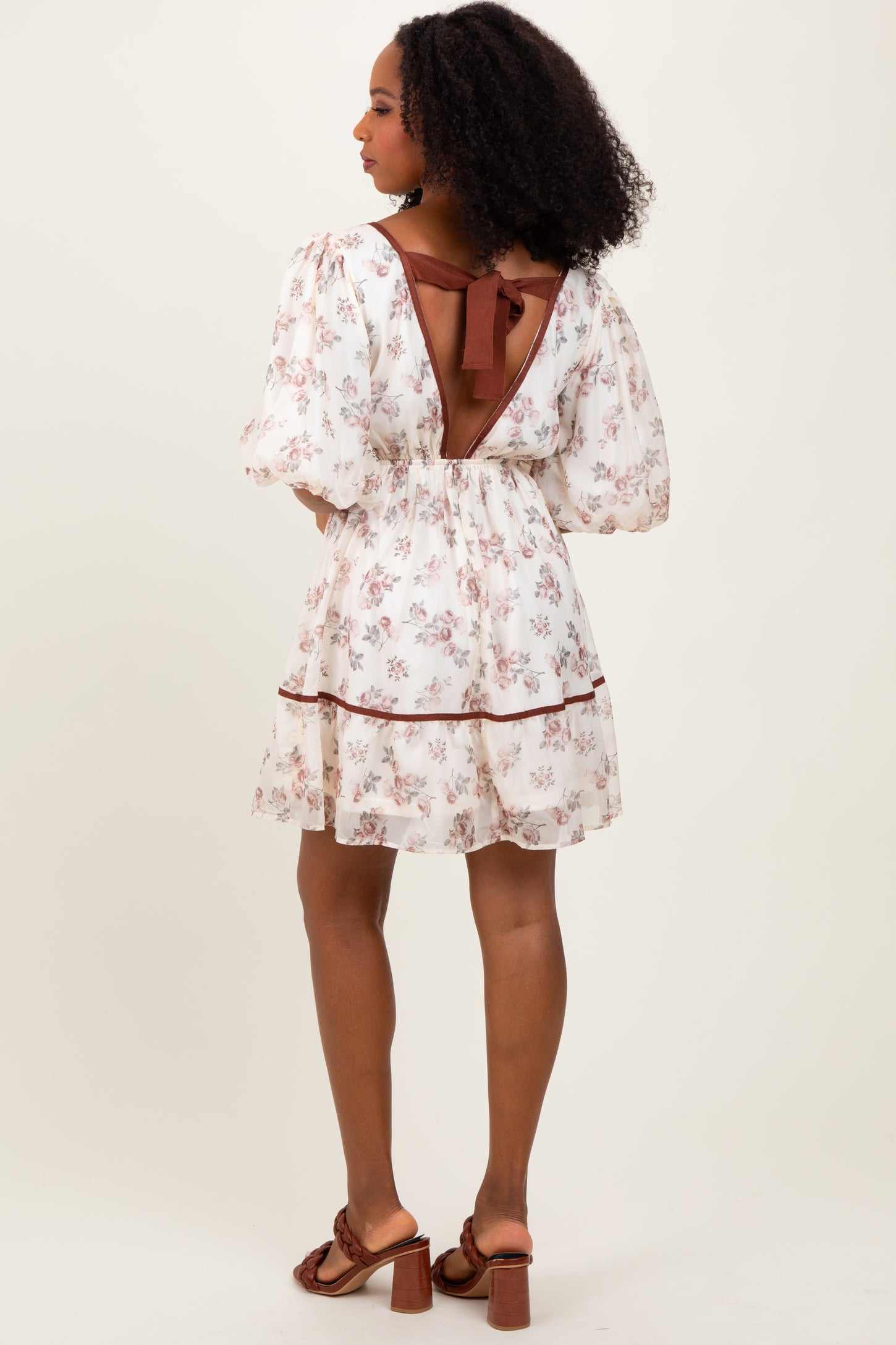 woman wearing a floral white short dress with puff sleeves and a back tie detail