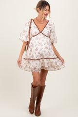 woman wearing a flowy white maternity dress with floral print and short puff sleeves, posing with a baby bump visible