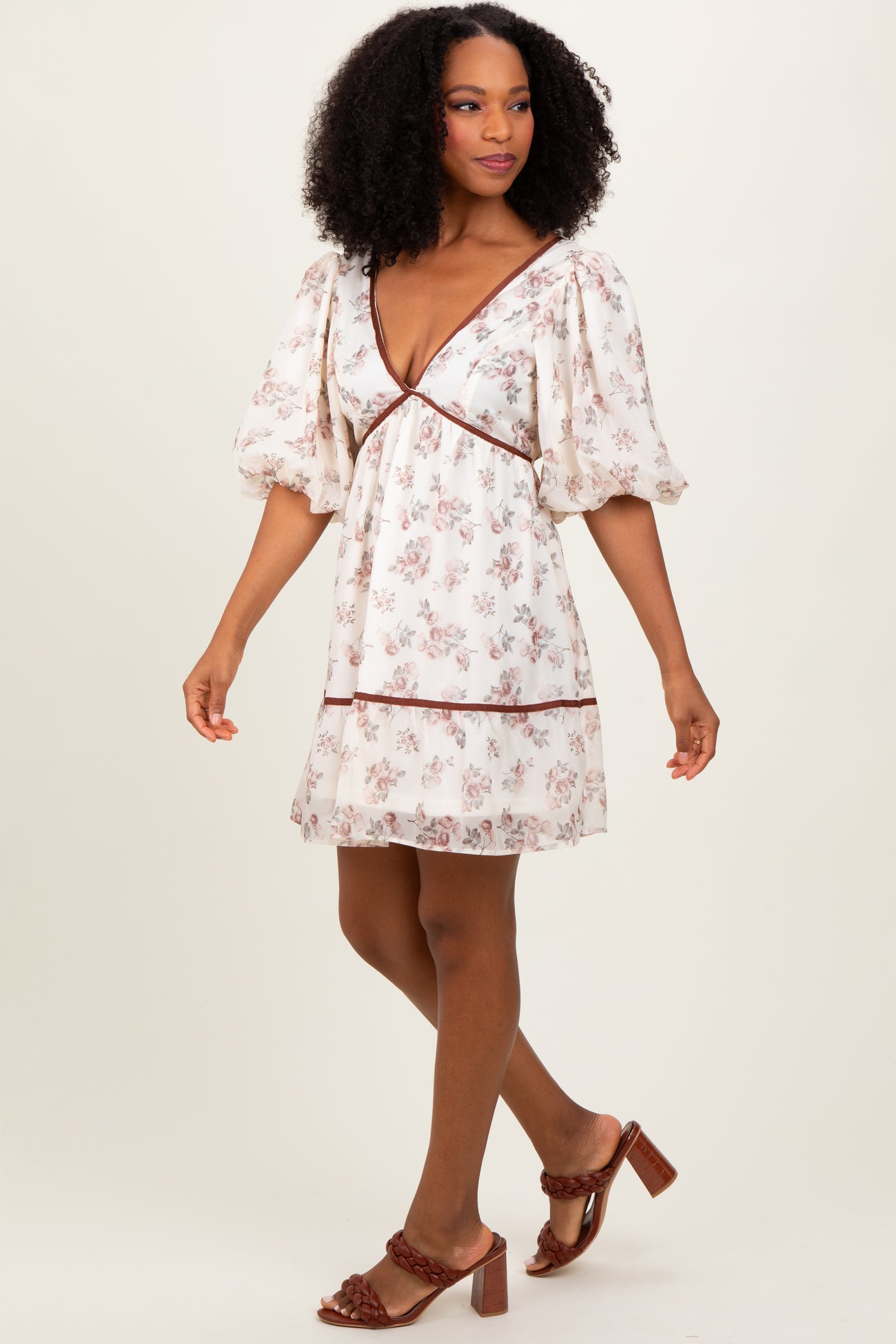 woman wearing a cream floral print puff sleeve dress with a v-neck and brown trim, paired with heeled sandals