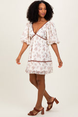 woman wearing a cream floral print puff sleeve dress with a v-neck and brown trim, paired with heeled sandals