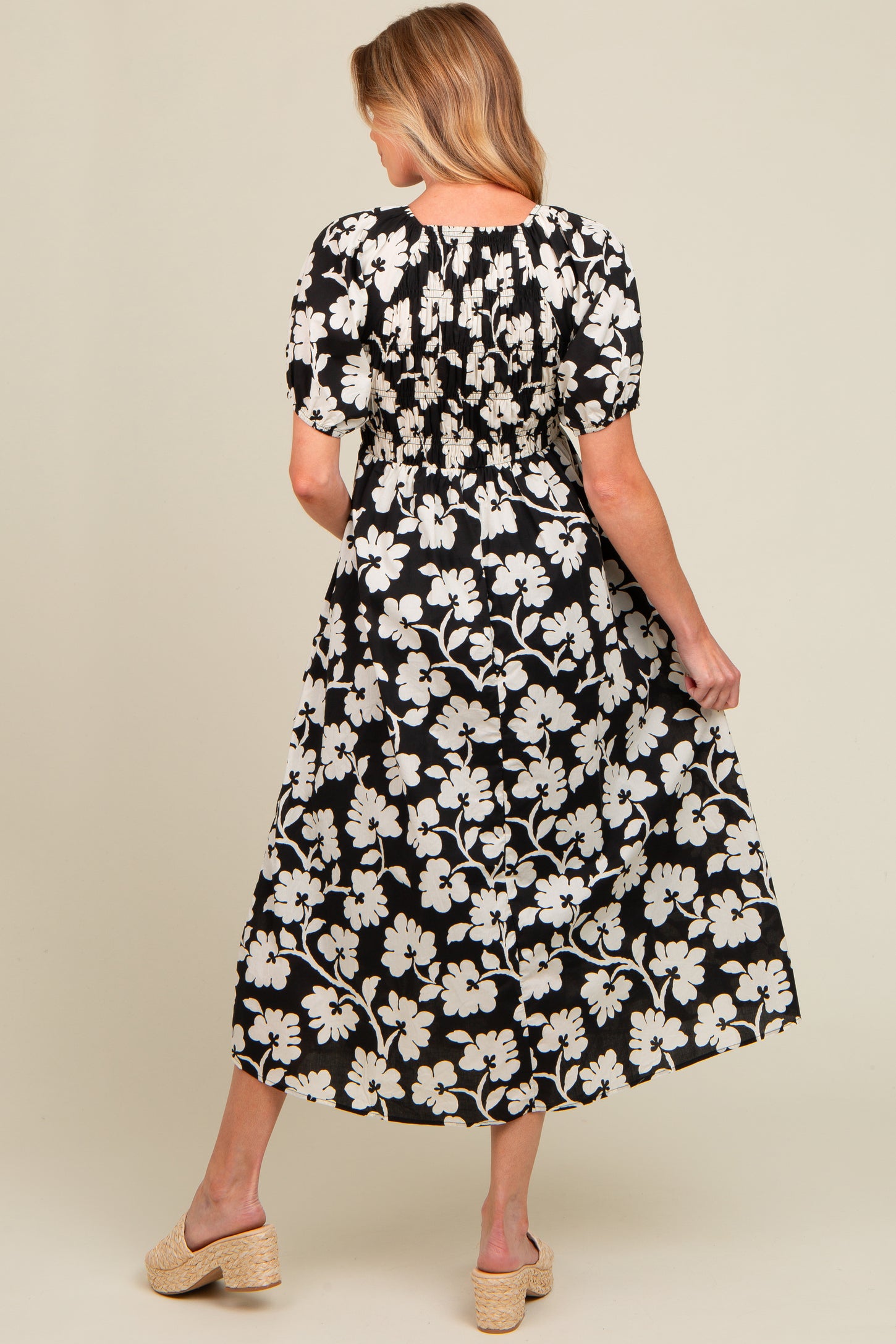 woman wearing a black floral maternity maxi dress with short puff sleeves, showing a smocked back and styled with wedges
