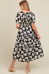 woman wearing a black floral maternity maxi dress with short puff sleeves, showing a smocked back and styled with wedges