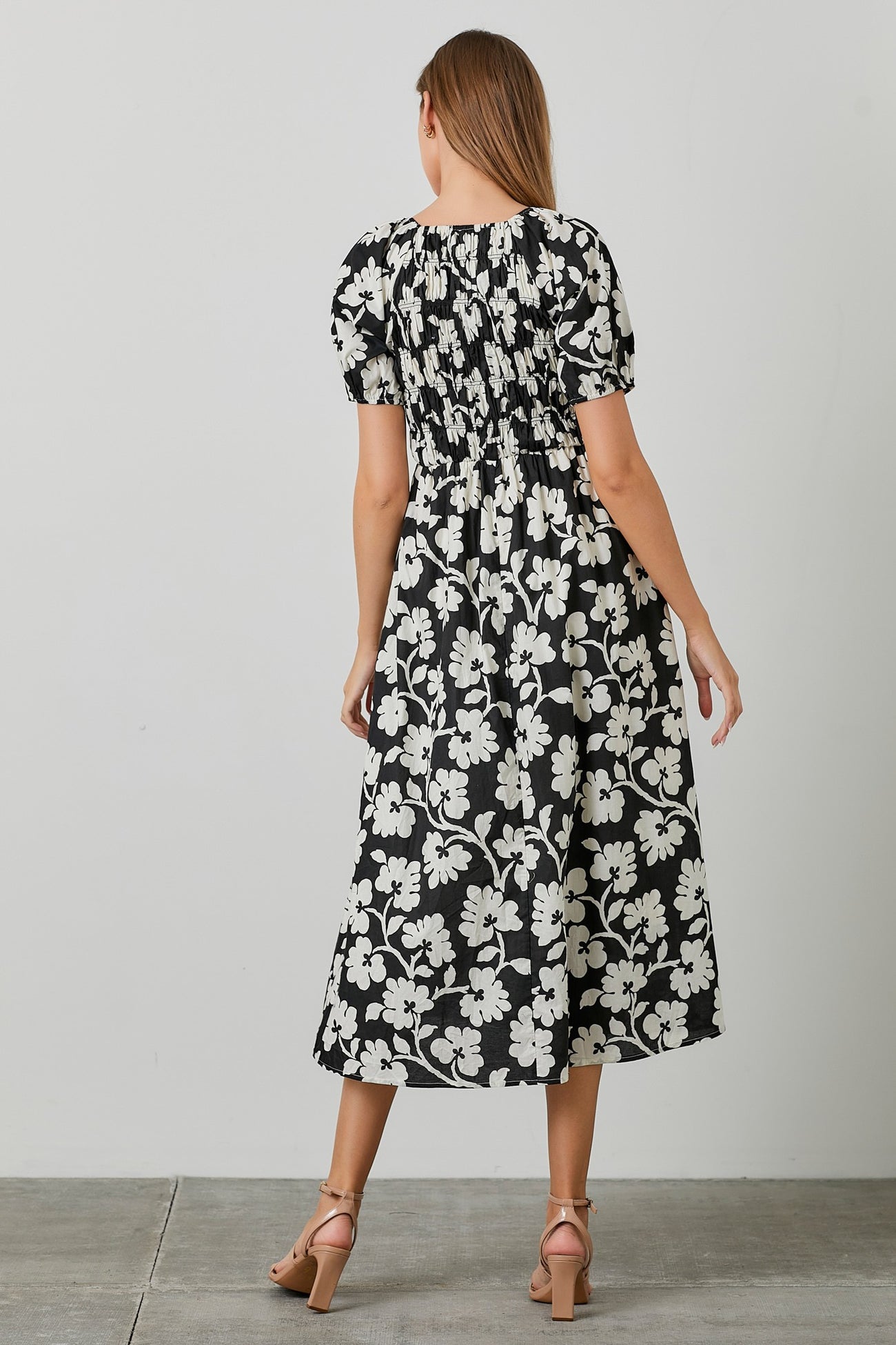 woman wearing a black and white floral midi dress with puff sleeves and a smocked waist seen from the back