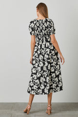 woman wearing a black and white floral midi dress with puff sleeves and a smocked waist seen from the back