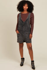woman wearing a dark wash denim overall dress with pockets over a brown long sleeve top and black ankle boots
