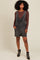 woman wearing a dark wash denim overall dress with pockets over a brown long sleeve top and black ankle boots