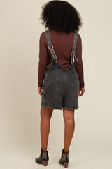 woman wearing a dark wash denim overall dress with a brown long sleeve top and black ankle boots from the back
