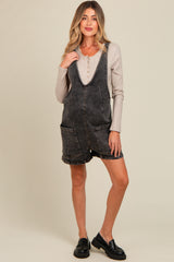 woman wearing a black denim maternity overall dress with pockets over a beige long sleeve top