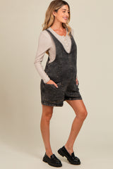 woman wearing a gray denim maternity romper with pockets and a beige long sleeve shirt, showing her baby bump