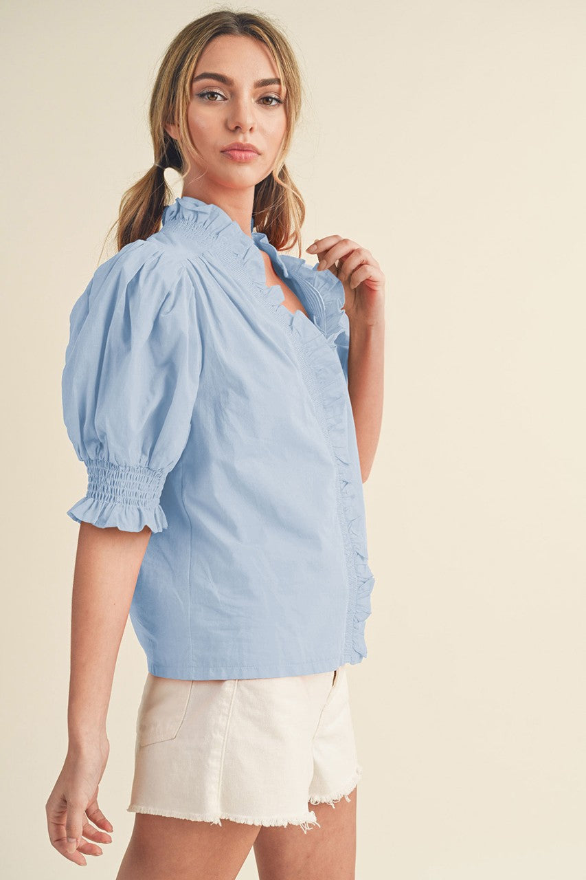 woman wearing a light blue puff sleeve blouse with ruffled detailing, paired with white shorts