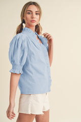woman wearing a light blue puff sleeve blouse with ruffled detailing, paired with white shorts