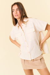 woman wearing a beige short sleeve button-up shirt with two chest pockets and a cream mini skirt