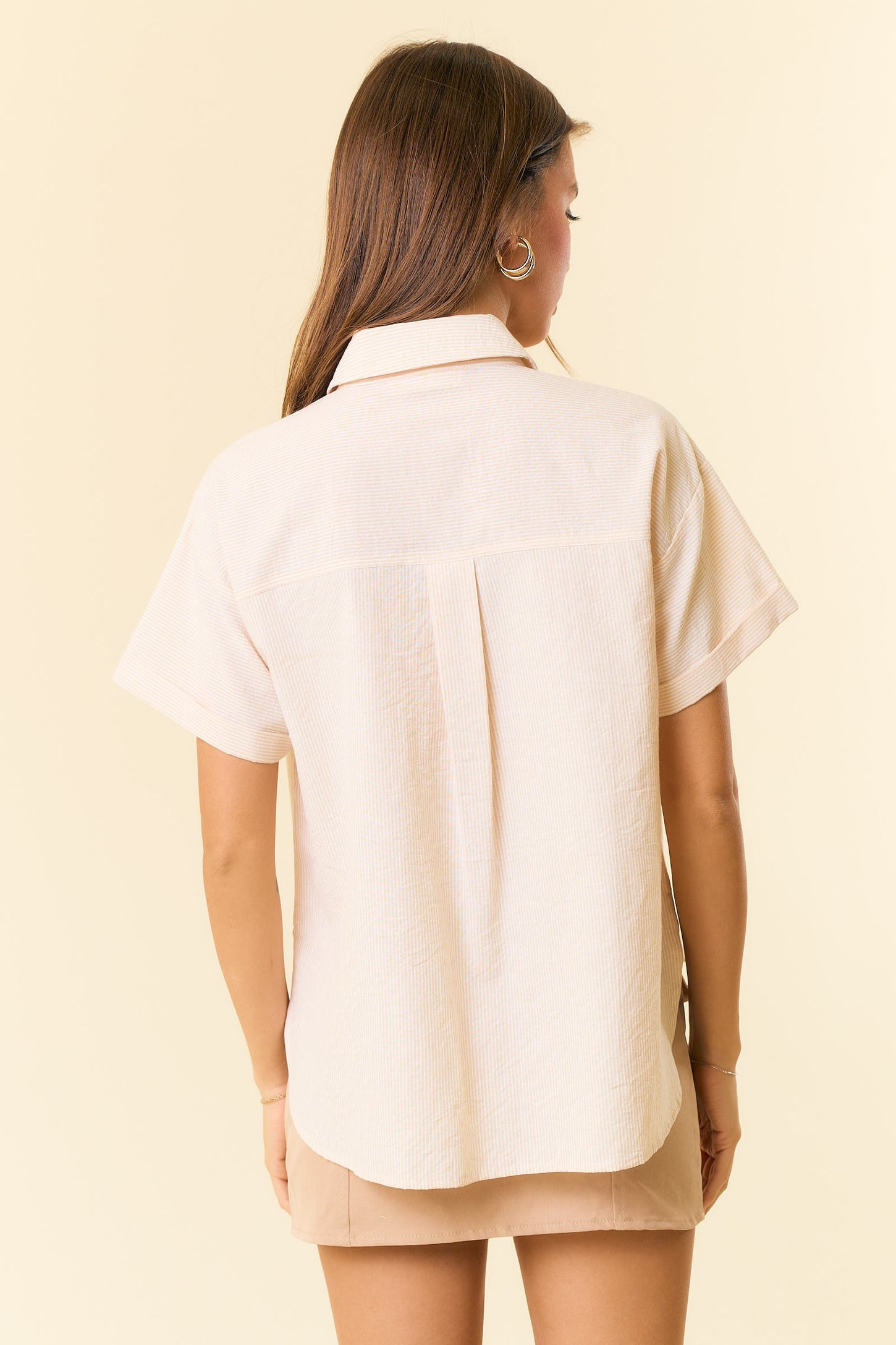 woman wearing a light beige short sleeve button-up shirt, seen from the back against a pale background