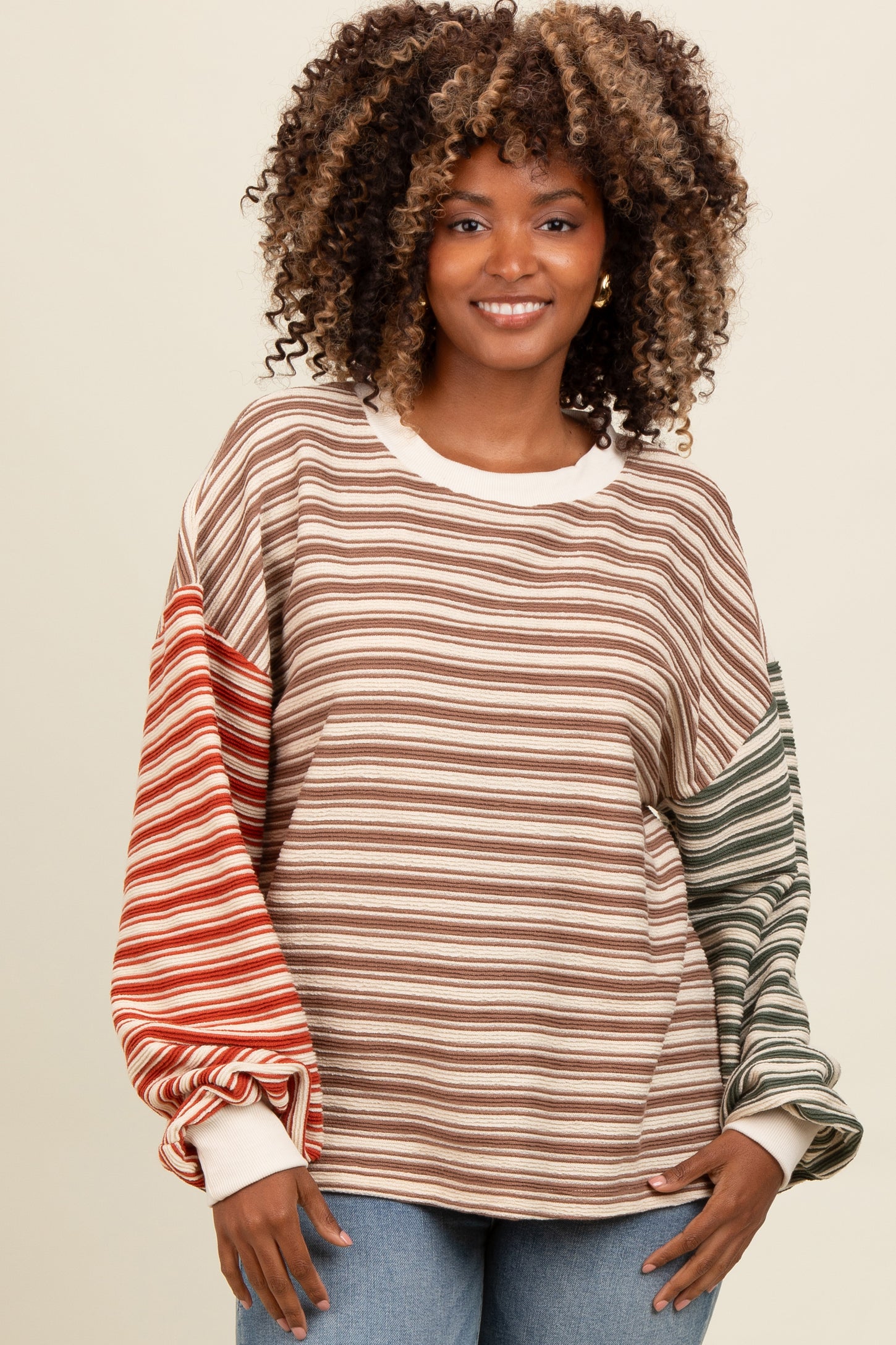woman wearing a striped oversized sweatshirt in brown, red, and green tones paired with light blue jeans