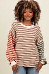 woman wearing a striped oversized sweatshirt in brown, red, and green tones paired with light blue jeans