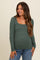 woman wearing a green long sleeve maternity top with a square neckline and a baby bump visible