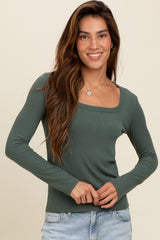 woman wearing a dark green ribbed long sleeve top with a square neckline and smiling at the camera