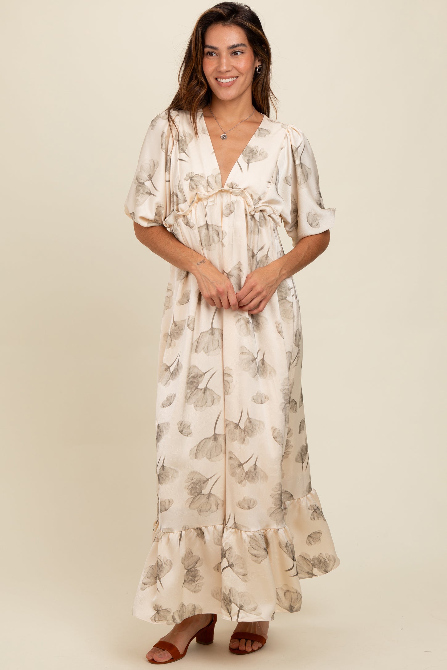 woman wearing a cream floral maxi dress with short sleeves and a ruffled hem, standing and smiling