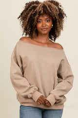 woman wearing a beige off-the-shoulder sweatshirt with long sleeves and relaxed fit, posing with hands clasped in front