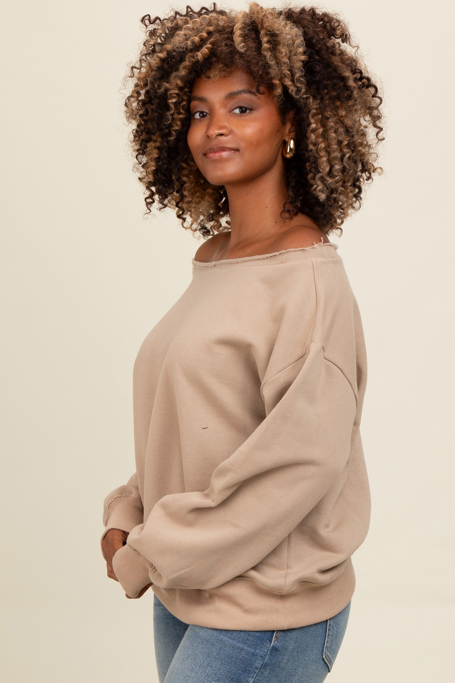 woman wearing a beige oversized sweatshirt with off-the-shoulder neckline and long sleeves, styled with blue jeans