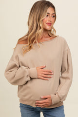 woman wearing a beige off-shoulder maternity sweatshirt and holding her baby bump