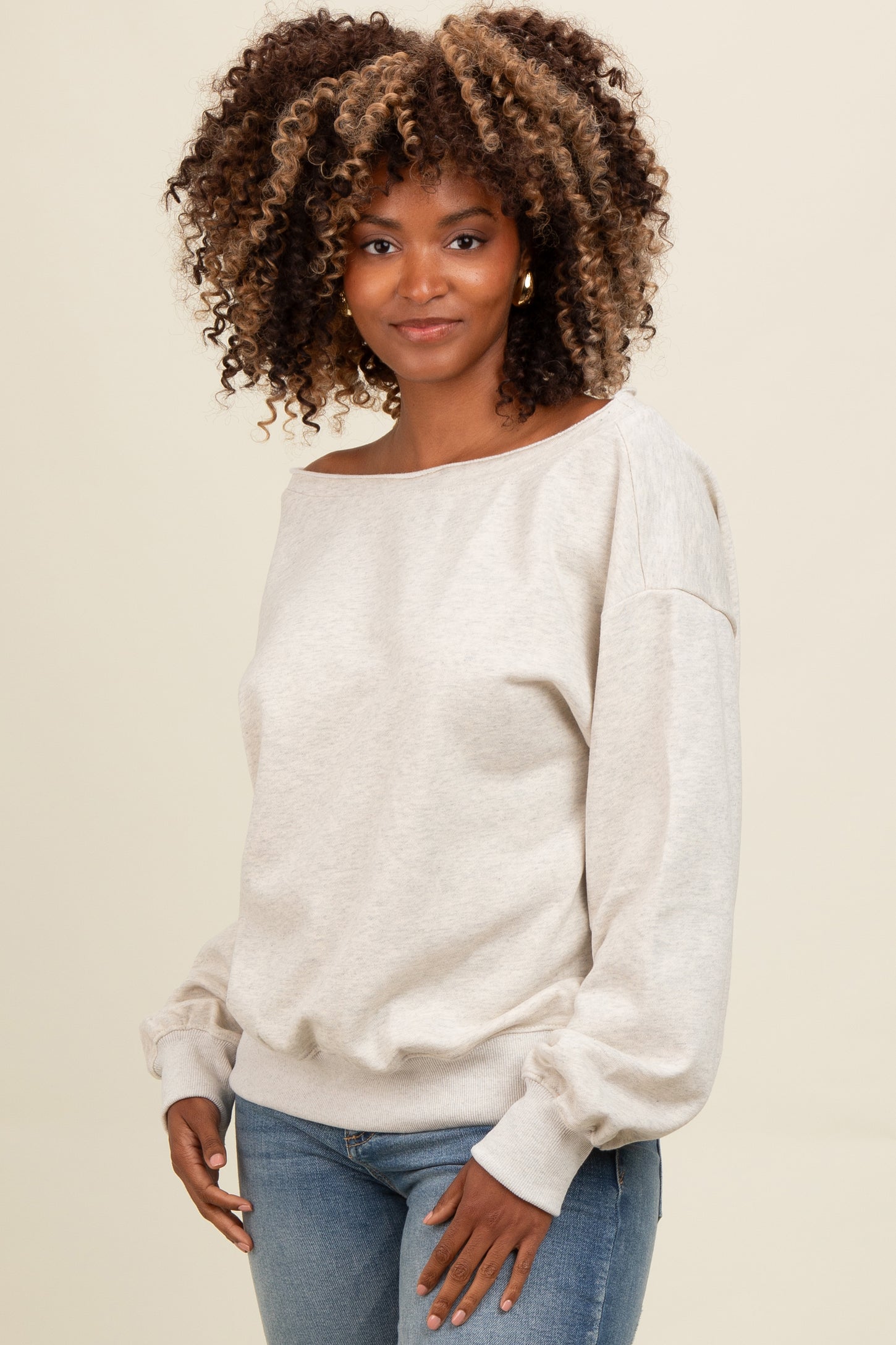 woman wearing a light beige off-the-shoulder sweater with balloon sleeves and light blue fitted jeans