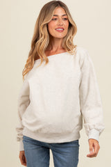 woman wearing a light gray maternity sweatshirt with a wide neckline and long sleeves, smiling at the camera