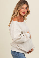 woman wearing a light gray oversized maternity sweatshirt and holding her baby bump