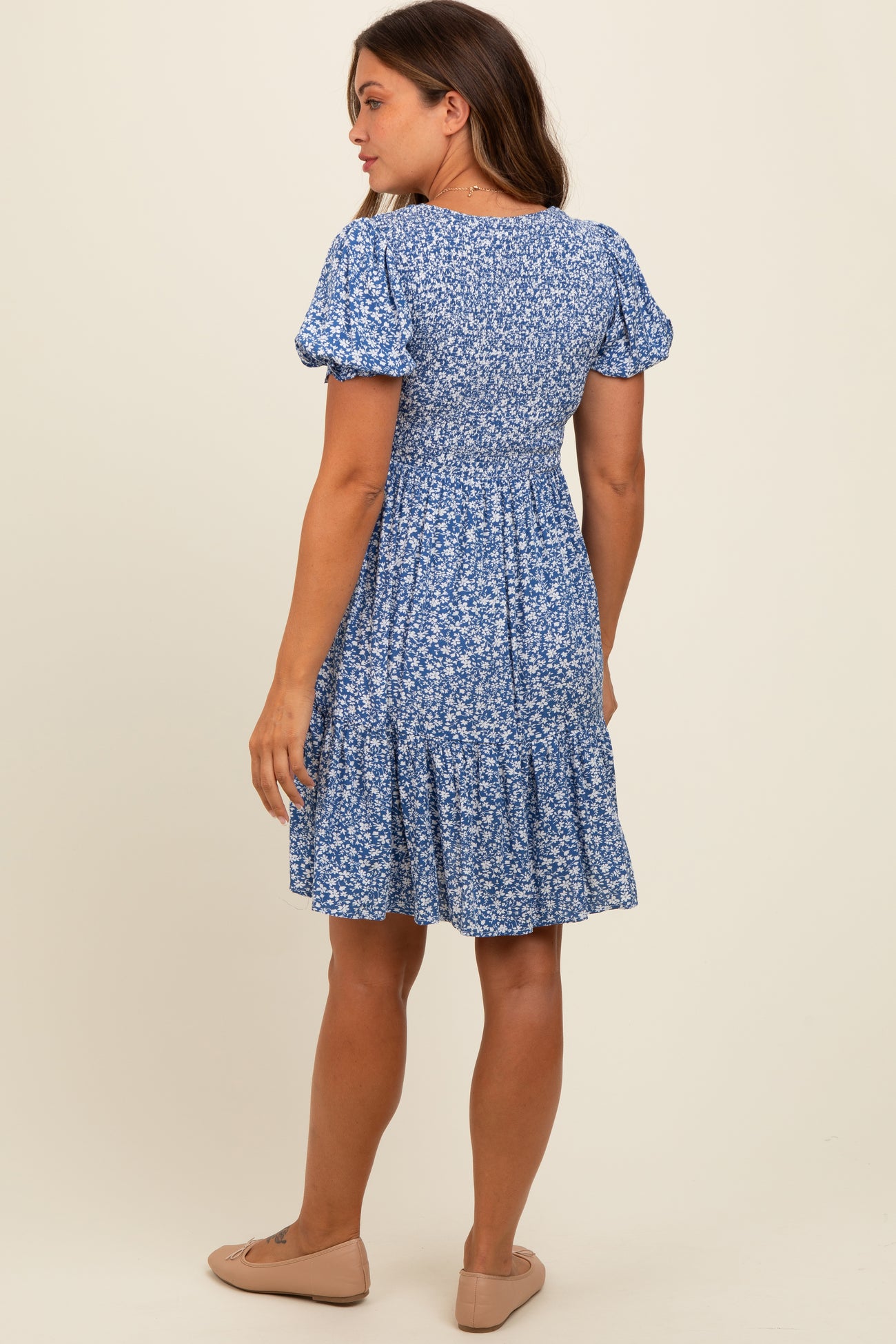 woman wearing a blue floral maternity dress with puff sleeves and a flared skirt, showing the back view