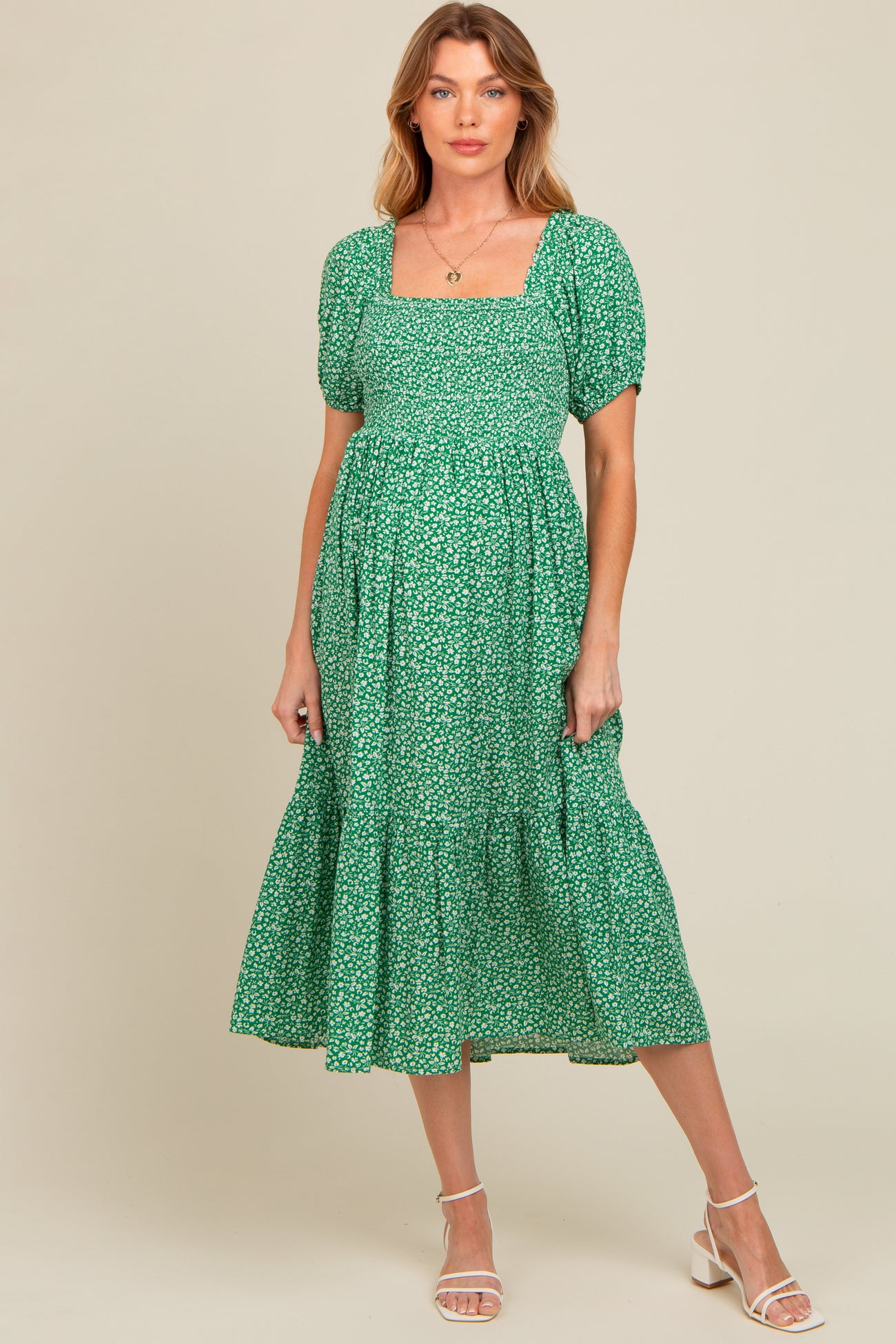 woman wearing a green floral maternity dress with short puff sleeves and a tiered skirt showcasing her baby bump