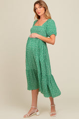 woman wearing a green floral maternity dress with short sleeves and a tiered skirt, holding her baby bump