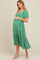 woman wearing a green floral maternity dress with short sleeves and a tiered skirt, holding her baby bump