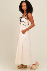 woman wearing a cream maxi dress with black drawstring details and pockets, paired with tan wedge sandals