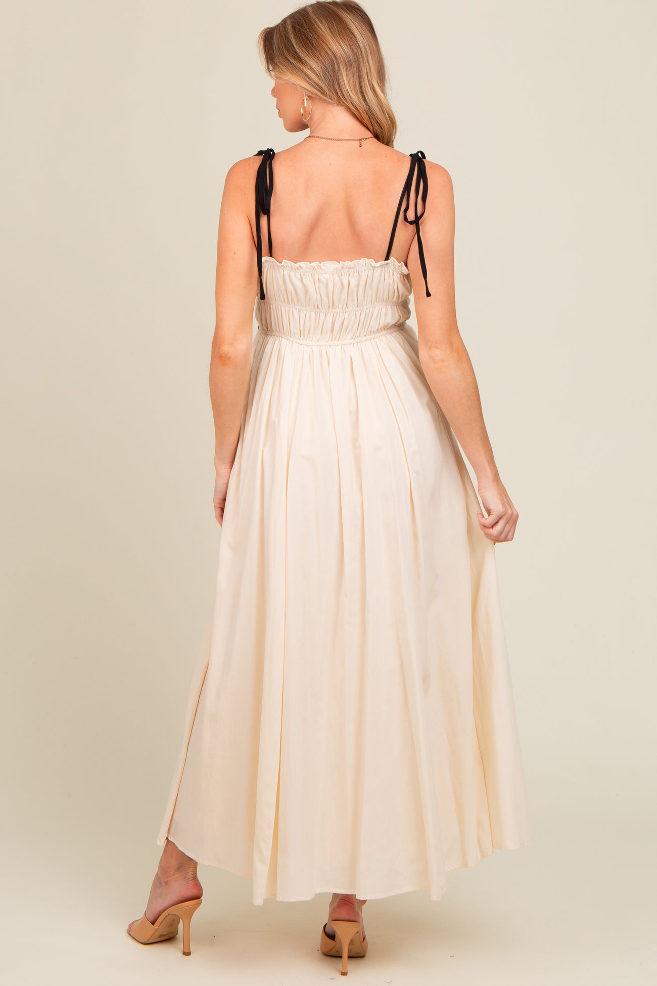 woman wearing a cream maternity maxi dress with adjustable black tie straps and a smocked back